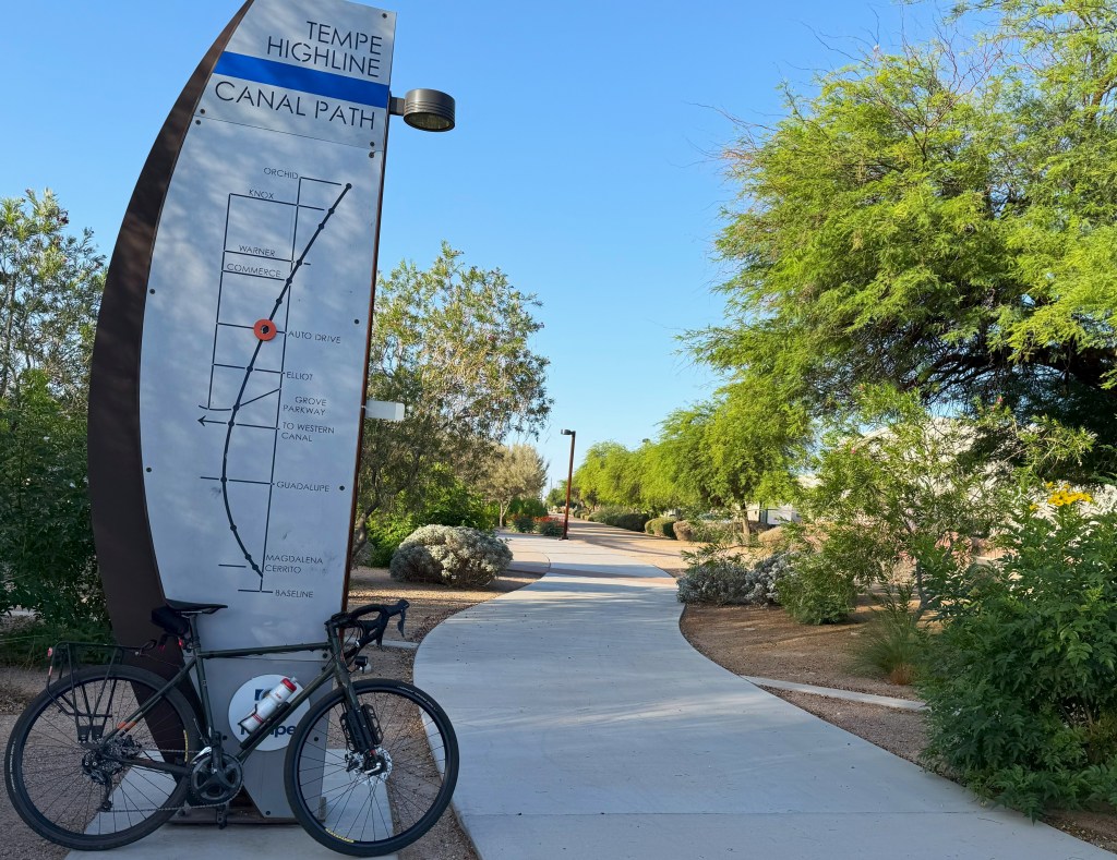 A bicycle leans against a wayfinding sign along a path.
