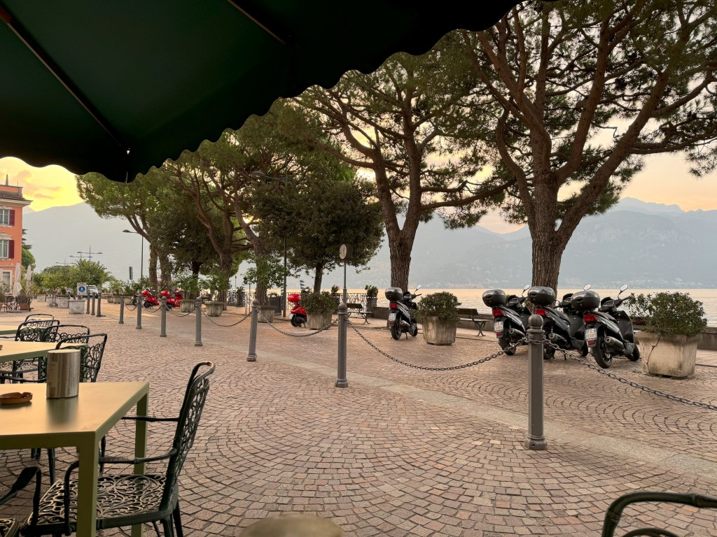 Scooters sit parked in a lakeside Italian city square.
