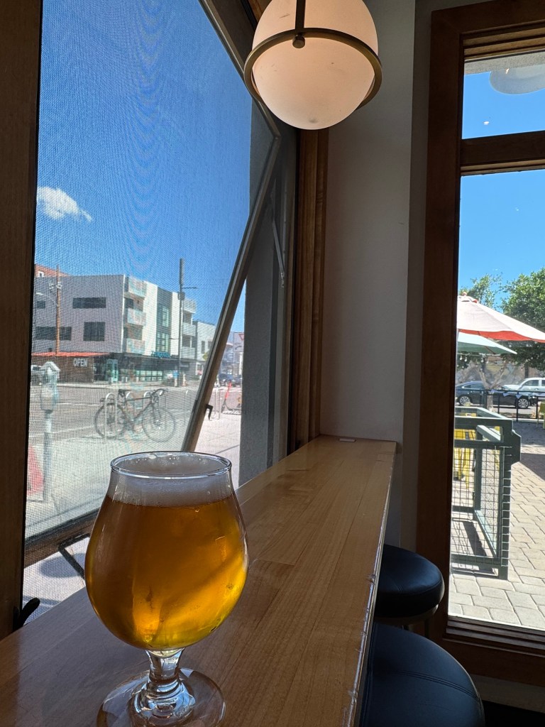 A beer on a table with a bicycle outside.