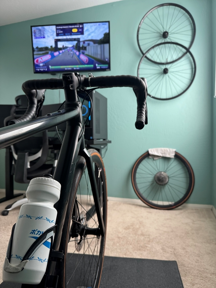A road bike sits on a Tacx indoor trainer facing a TV