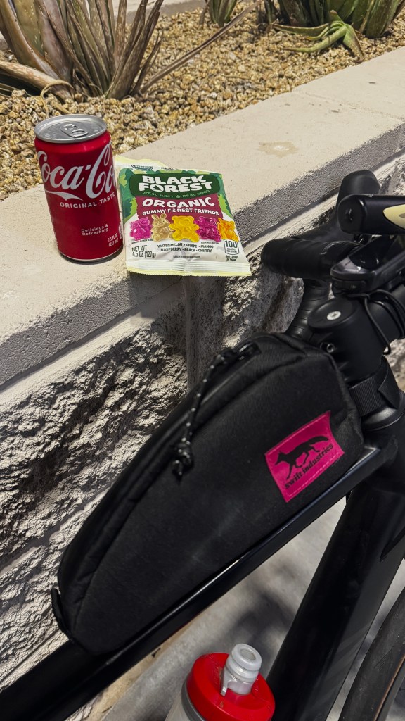 A can of Coca Cola and a bag of gummy bears next to a bicycle.